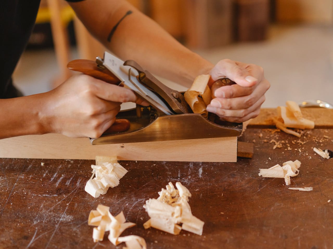 Menuisier ajustant une pièce de bois au rabot, copeaux sur l'établi