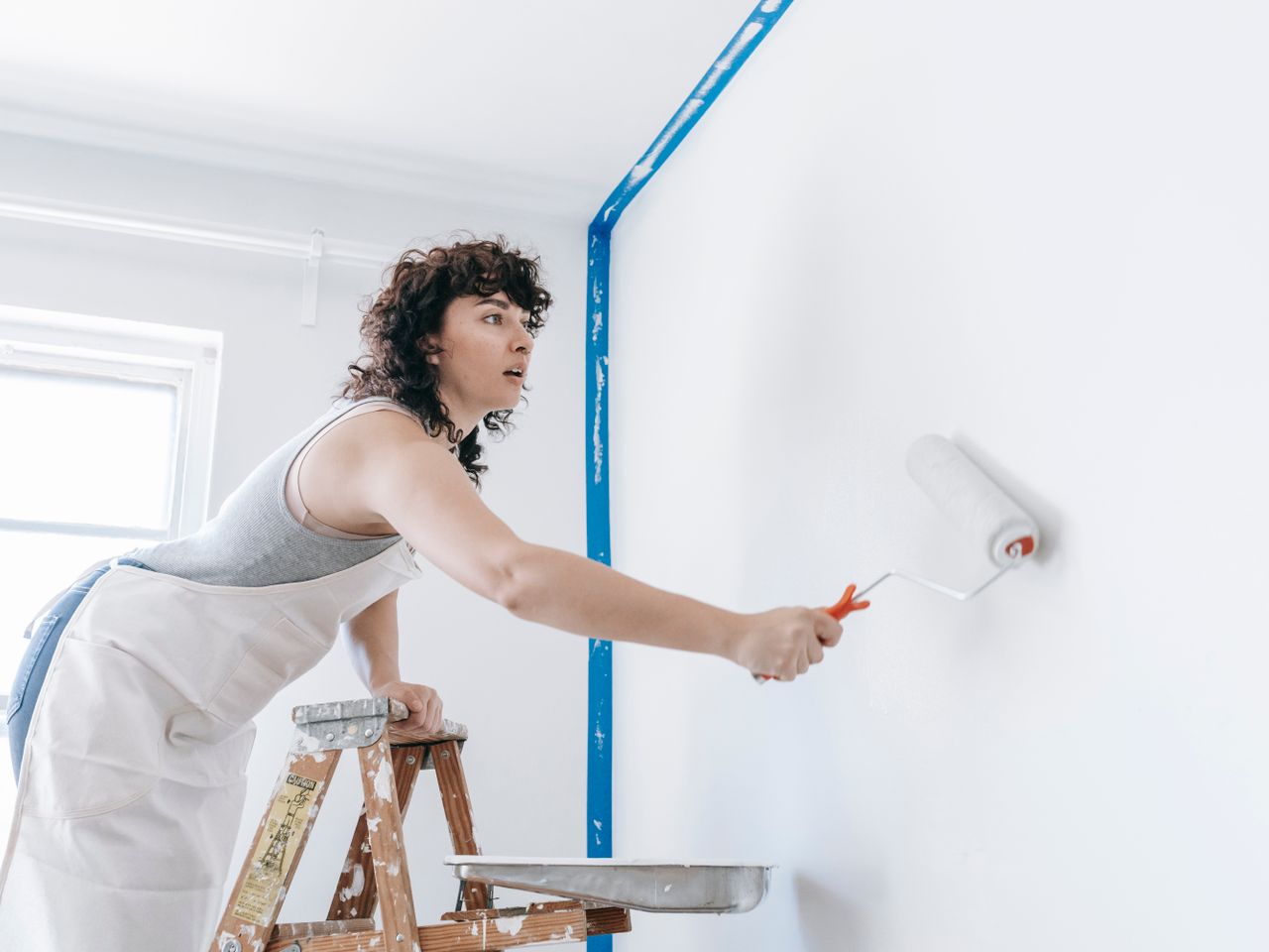 Peintre en tenue de travail peignant un mur depuis un escabeau